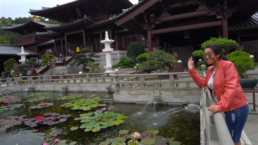 Meenu waving from the railing of a lily pond, with Chi Lin Nunnery's timber halls behind