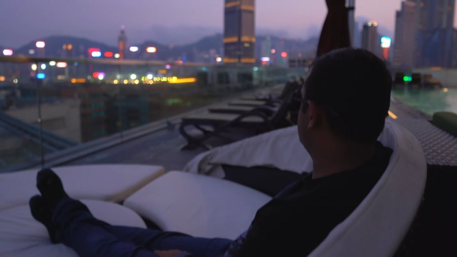 Praddy stretched out on a daybed on our hotel's rooftop at dusk, with the city lights beyond