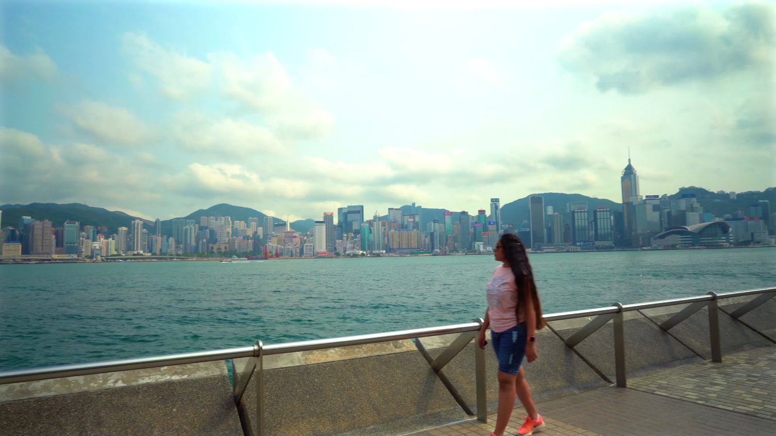 Meenu at the railing of the Tsim Sha Tsui promenade, looking across the harbour to Hong Kong Island