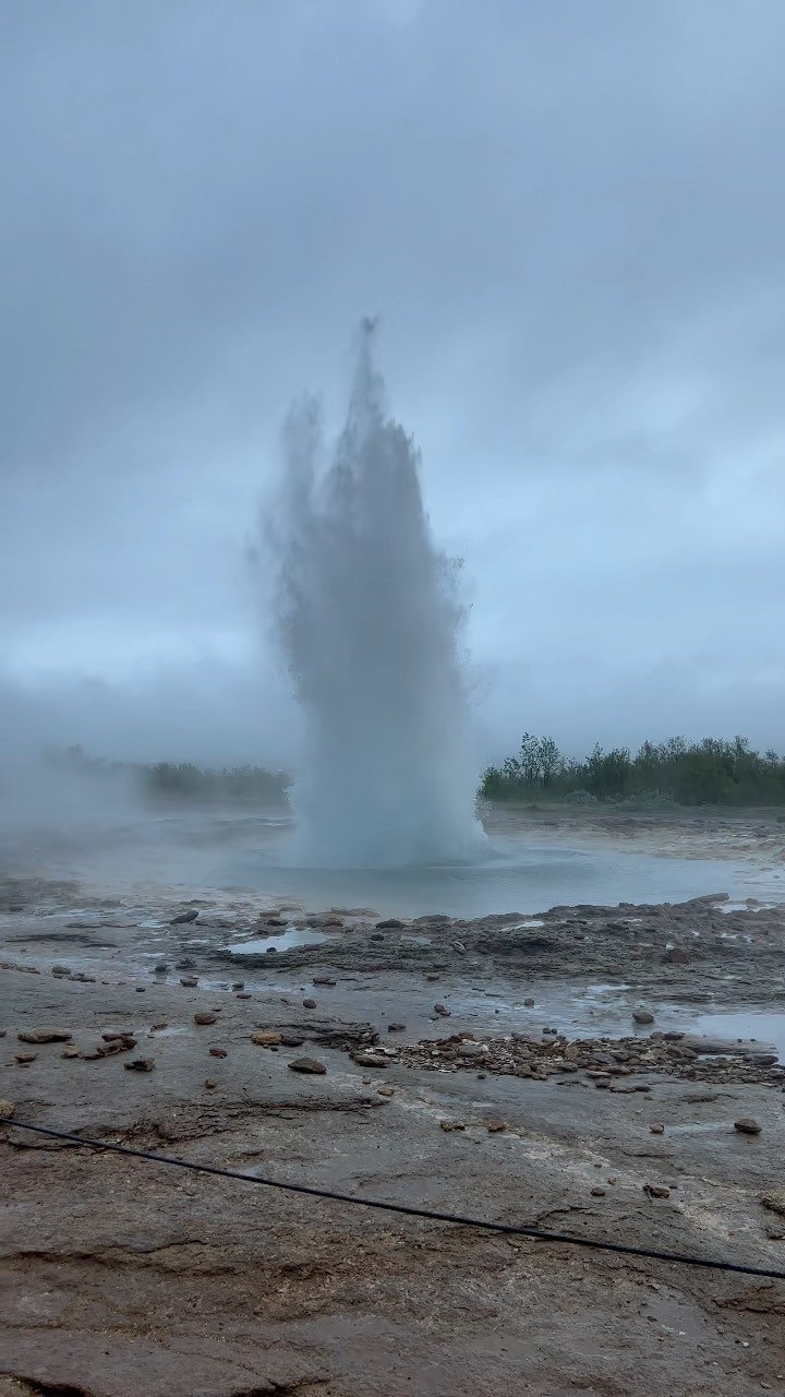 A geyser at Geysir throwing a column of water and steam into a grey sky