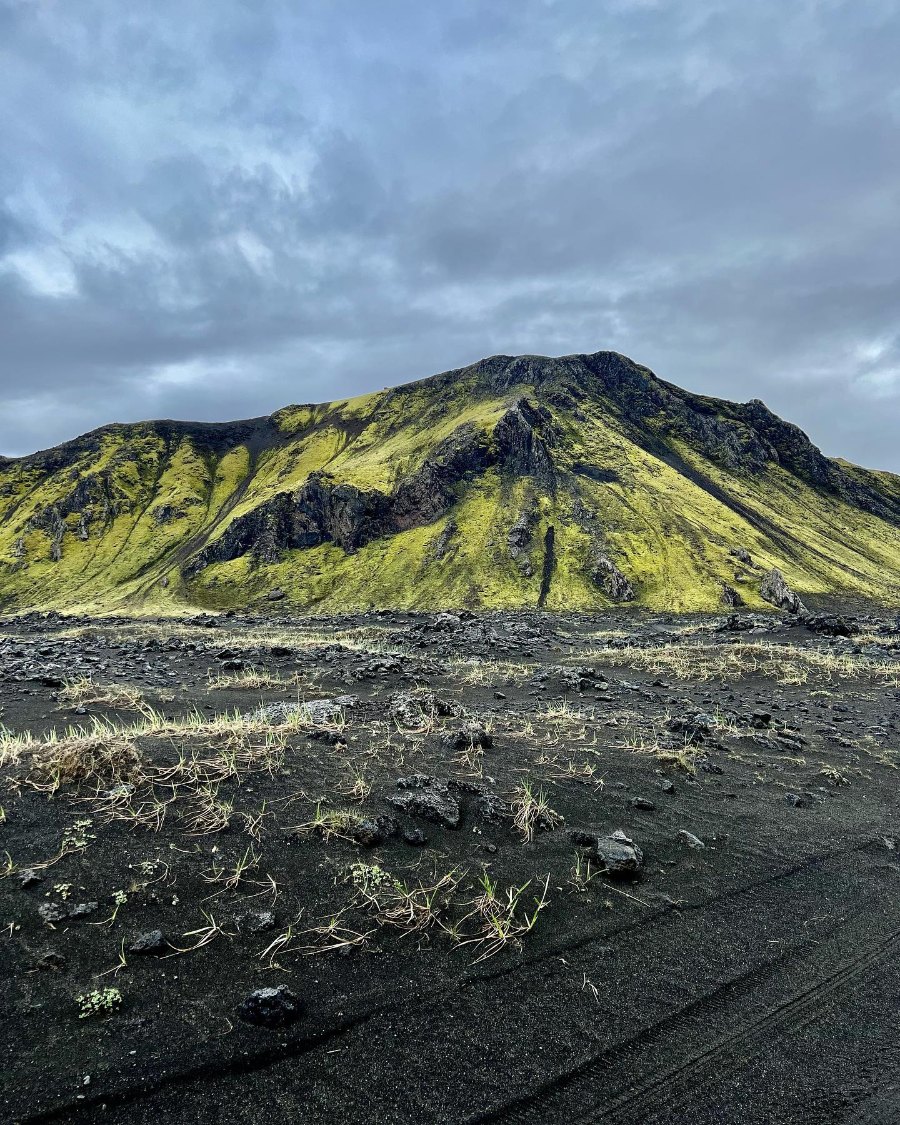 A mountain covered in bright green moss above a plain of black sand