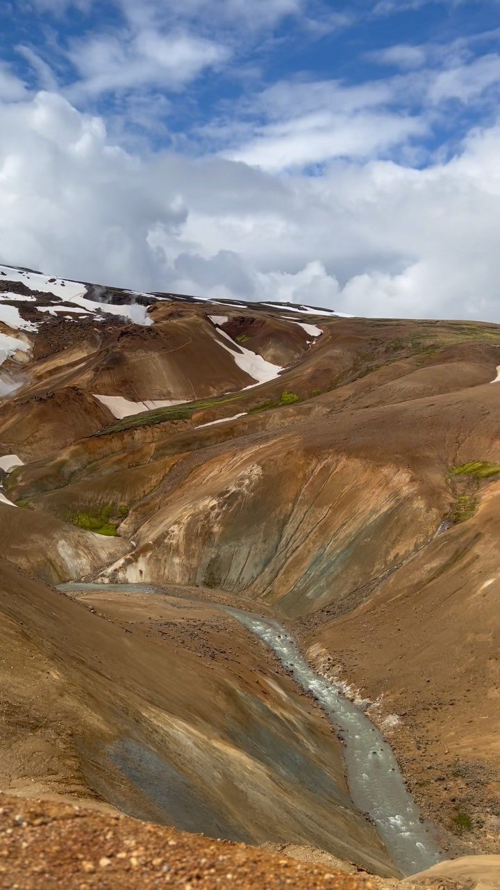A milky stream running down a valley of rust and ochre hills at Kerlingarfjöll, with snow on the tops