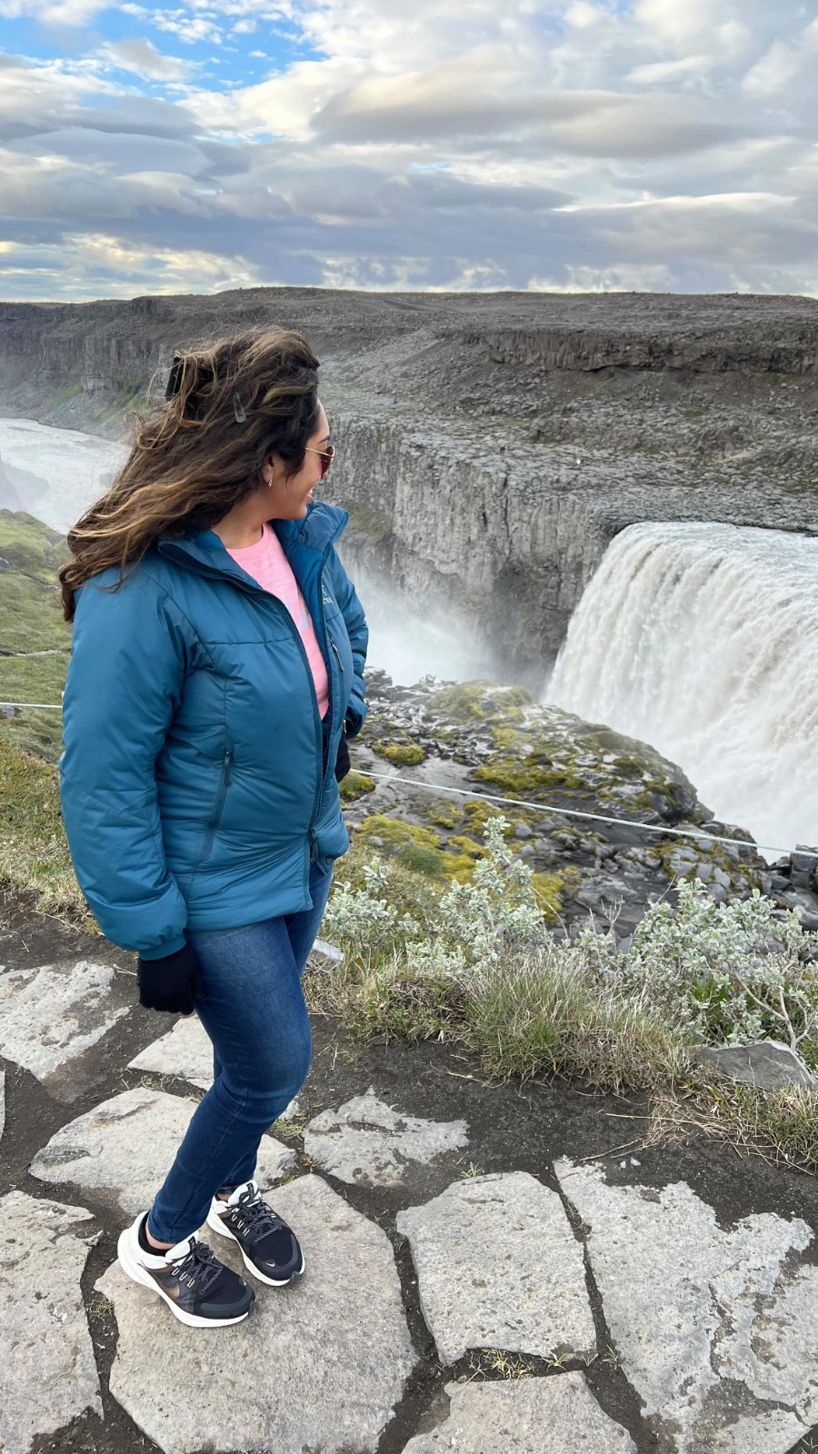 Meenu on the rocks above Dettifoss, with spray rising from the falls behind her