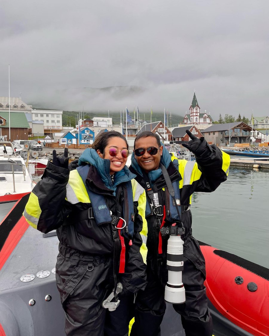 Meenu and Praddy waving in flotation suits on a red RIB in Húsavík harbour, with the church spire behind them