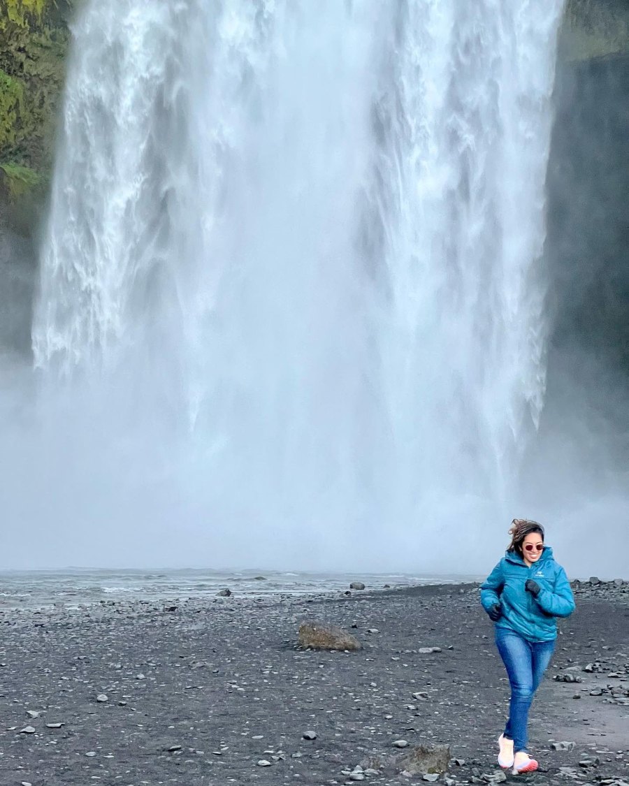 Meenu small at the foot of Skógafoss, its white water filling the frame behind her