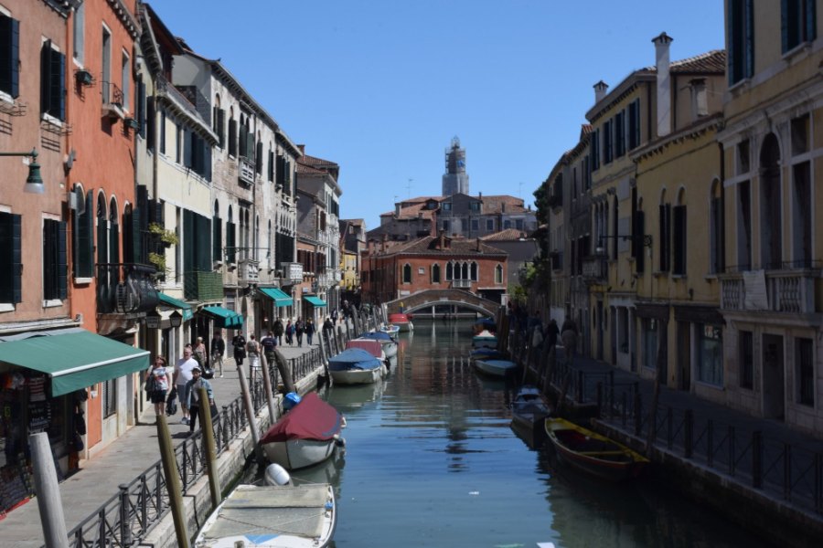 A quiet side canal lined with moored boats, with a footbridge further along