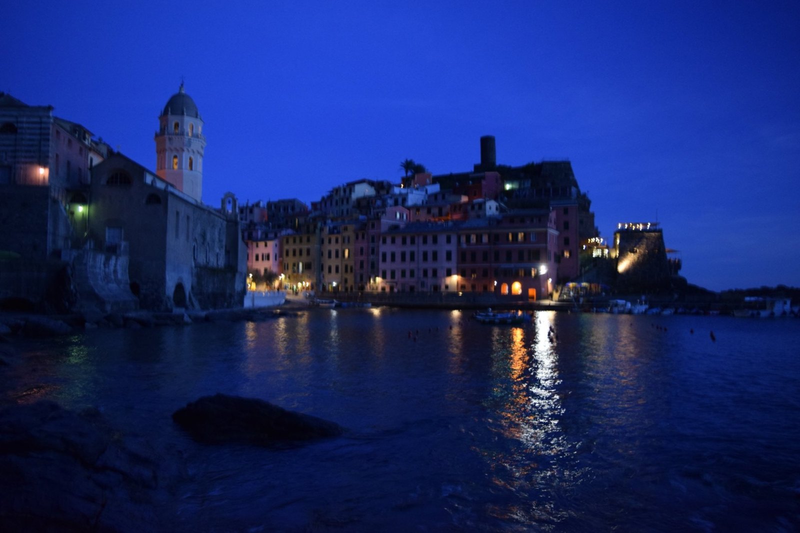 Vernazza's harbour at blue hour, the church tower and houses lit up and their lights reflected in the water