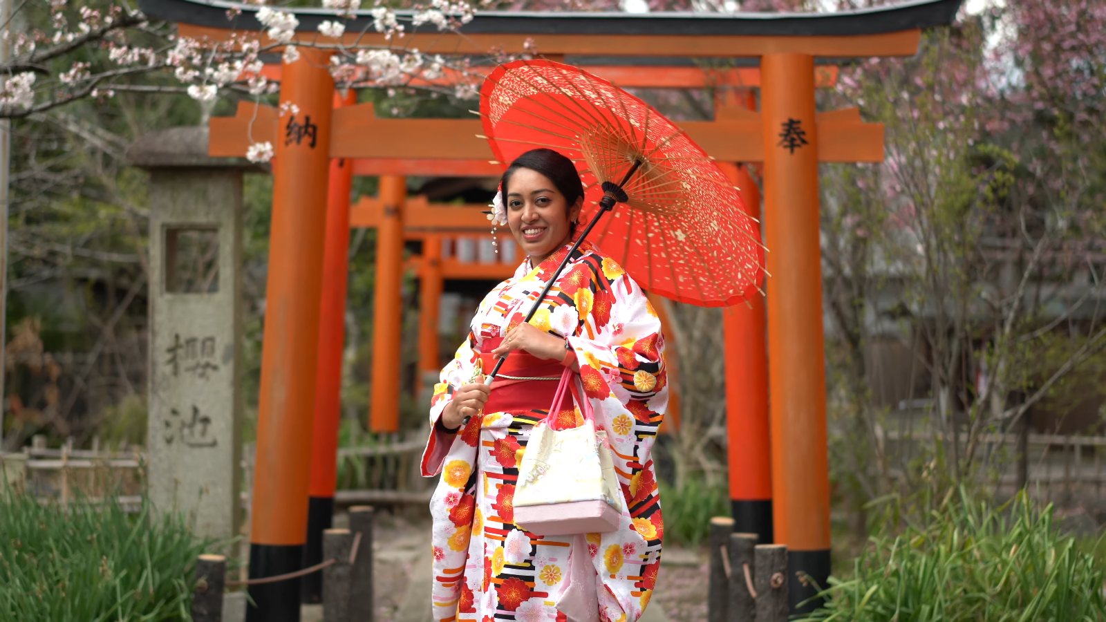 Meenu in a kimono with a red paper umbrella beneath vermilion torii gates