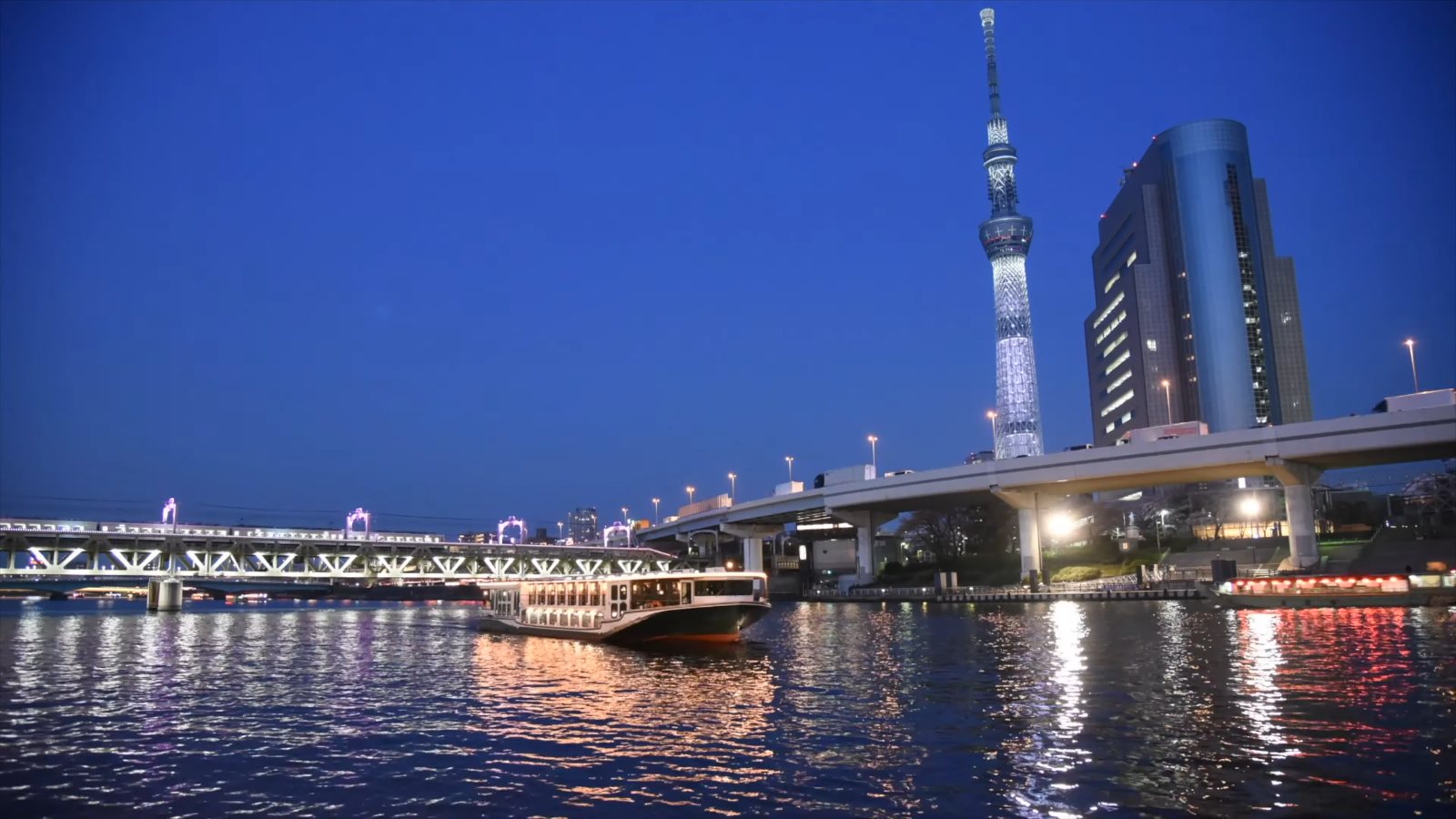 Tokyo Skytree over the Sumida River at dusk, with a lit boat on the water