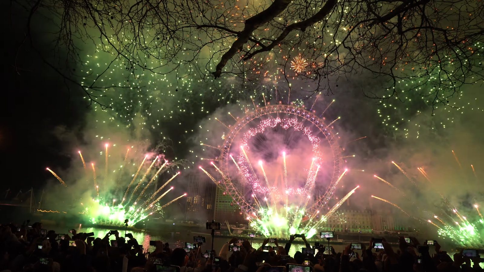 Green sparks filling the sky over the London Eye, lit pink, with green fountains along the river and phones raised in the crowd