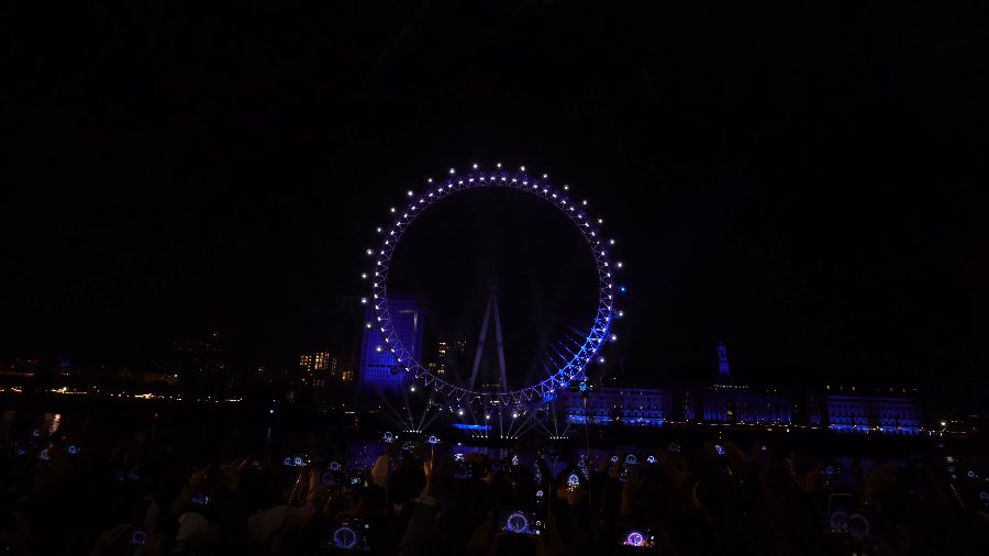 The London Eye glowing blue across the dark river just before midnight, with the crowd in silhouette
