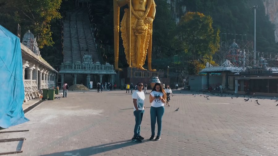 Drone view of the two of us standing below the giant golden statue of Lord Murugan and the steps up to Batu Caves