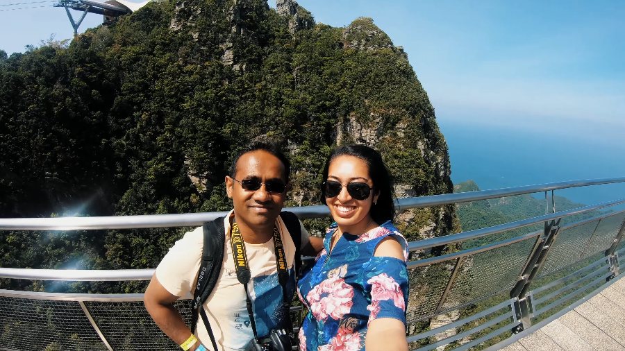 Praddy and Meenu taking a selfie on the SkyBridge, with a forested cliff and the sea behind