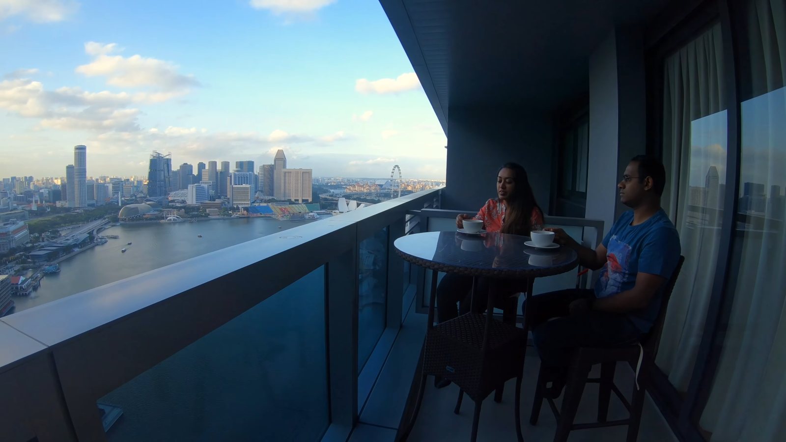 Meenu and Praddy at a table on our balcony, high above Marina Bay with the city skyline across the water