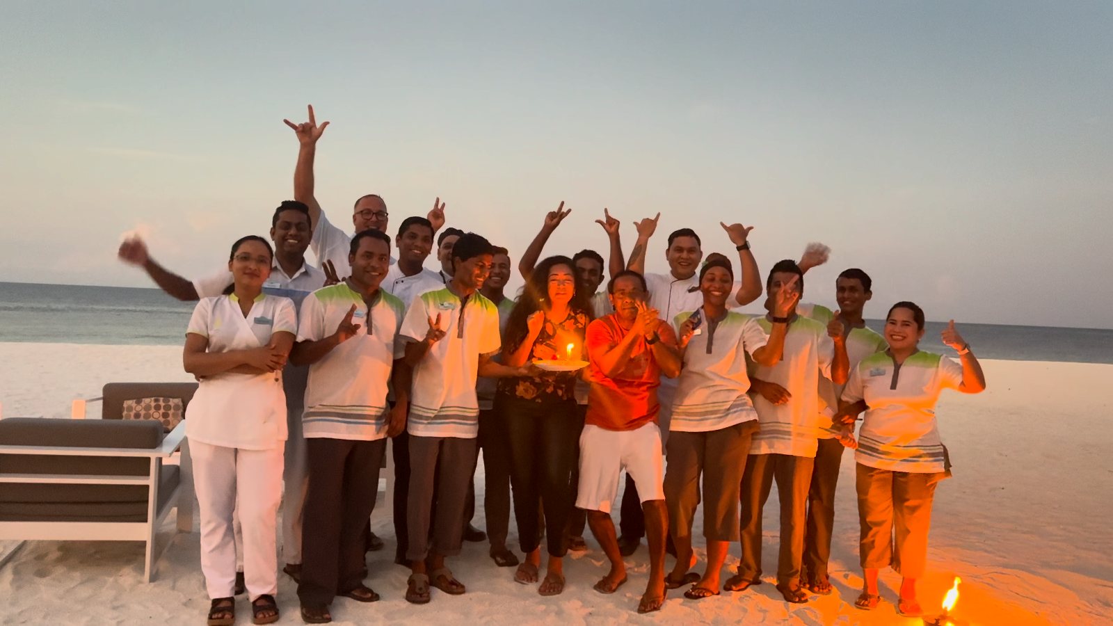 The Kandolhu team cheering on the beach at sunset around us and a candlelit cake