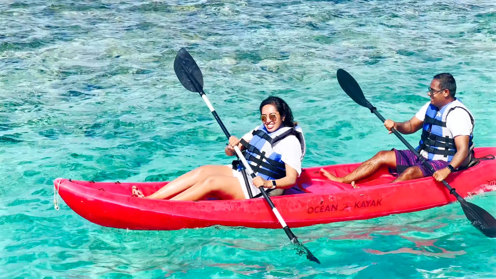 Meenu and Praddy paddling a red kayak over clear turquoise water
