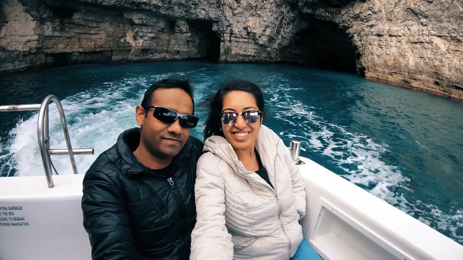 Meenu and Praddy in padded jackets on a speedboat, with sea caves behind