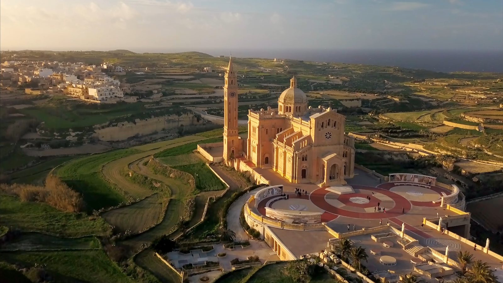 Ta' Pinu basilica and its bell tower among the fields in the late afternoon light, from the drone