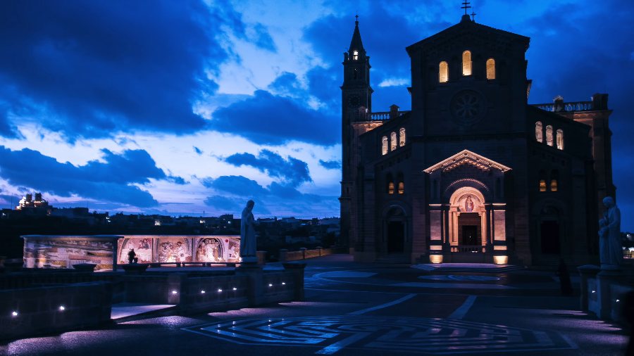 Ta' Pinu lit up after dark, under a deep blue sky