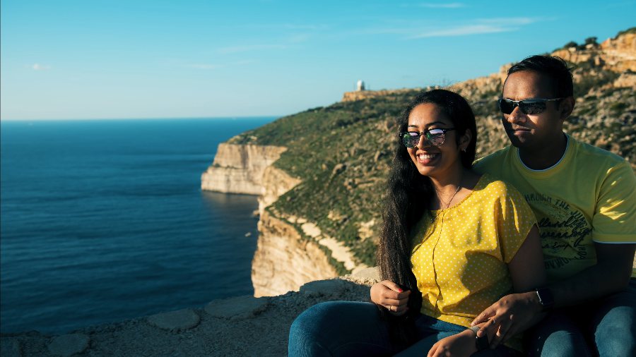 Meenu and Praddy sitting on a clifftop, with sea cliffs and a watchtower on the headland behind