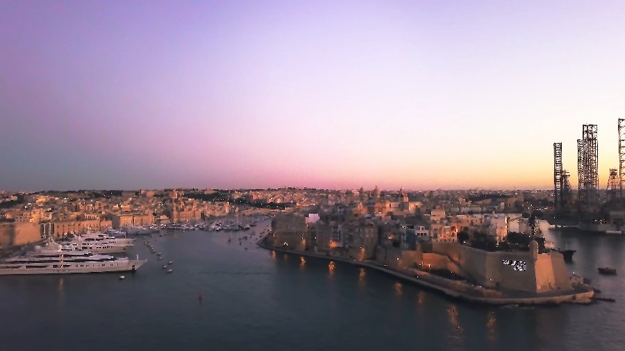 The Three Cities at dusk under a pink sky, with superyachts moored below the bastions