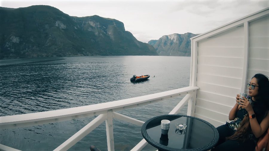Meenu on our cabin balcony over the still fjord, with a red boat on the water