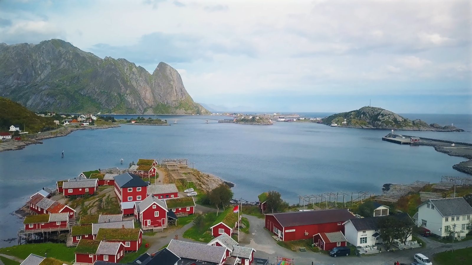 Drone view of red fishermen's cabins beside a bay in Lofoten, with jagged peaks behind