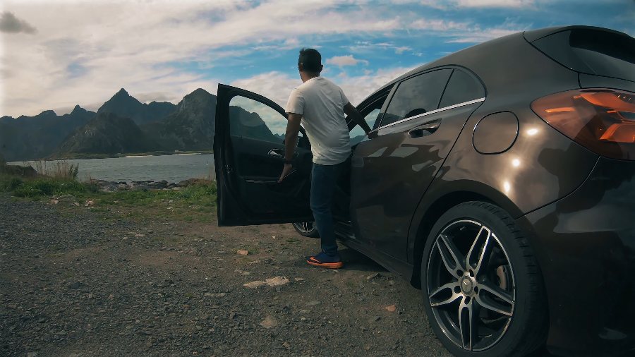 Praddy at the open door of our hire car, with peaks across the water