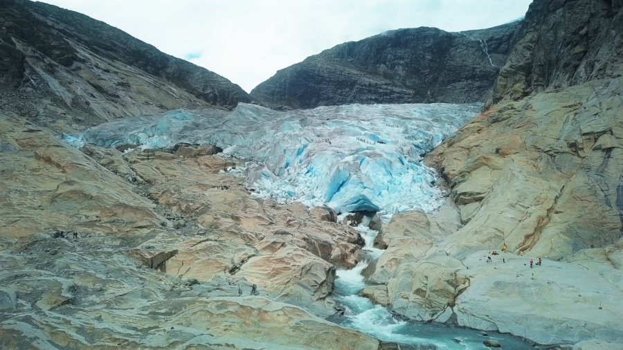 Drone view of the glacier's blue front, with its meltwater river running out over bare rock