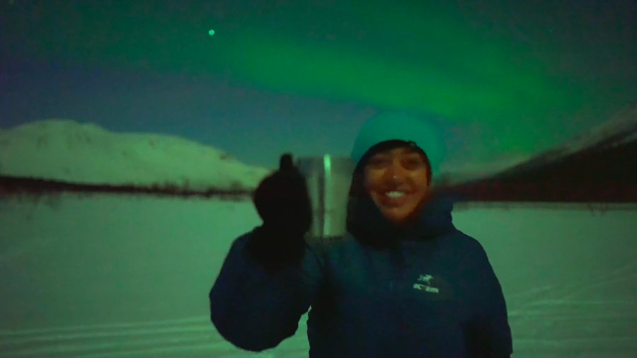 Meenu raising a cup under the green aurora