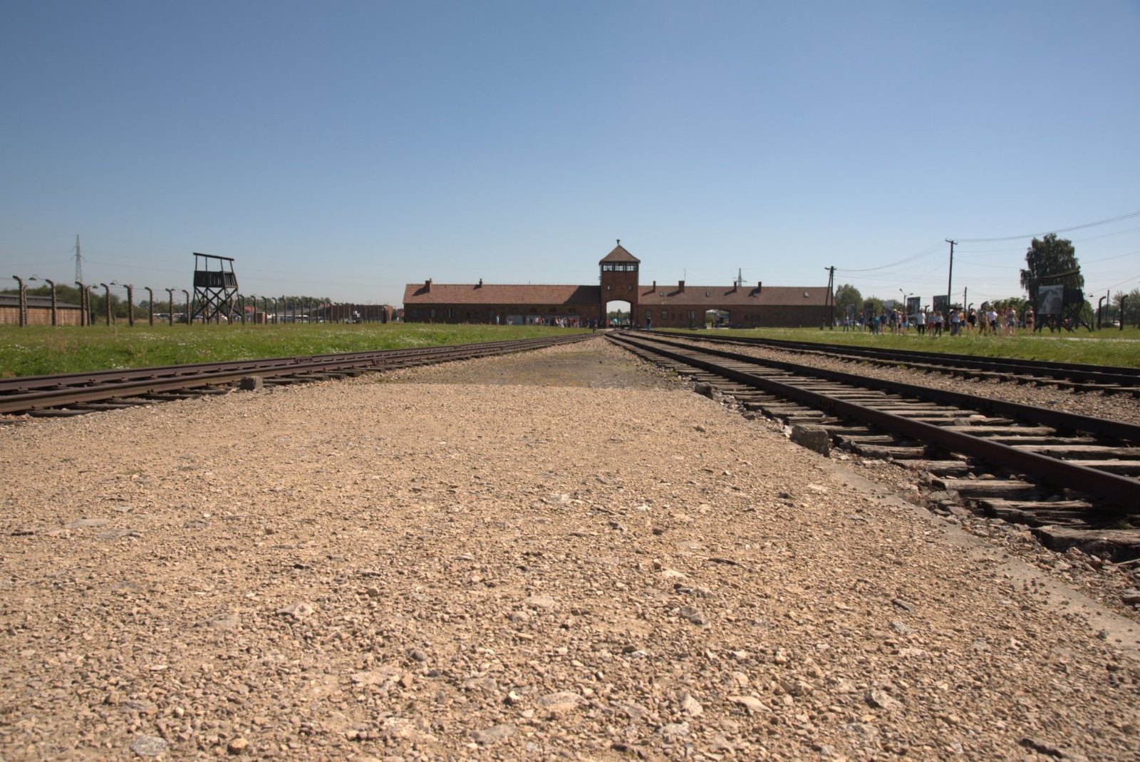The railway line at Birkenau running back to the long brick gatehouse under a clear sky