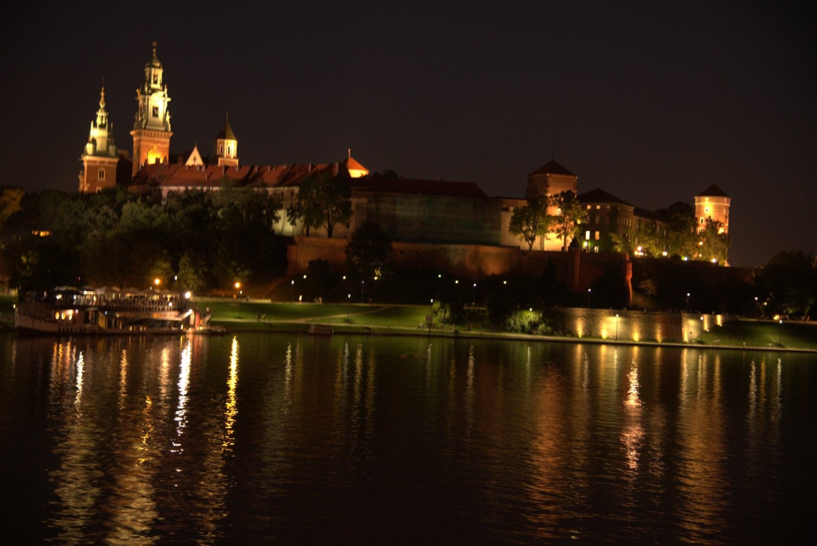 Wawel's castle and cathedral lit up on their hill at night, reflected in the Vistula