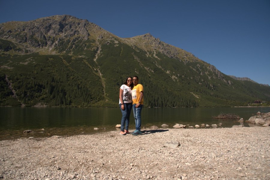 Meenu and Praddy on the stony shore of Morskie Oko, with a green mountainside behind them
