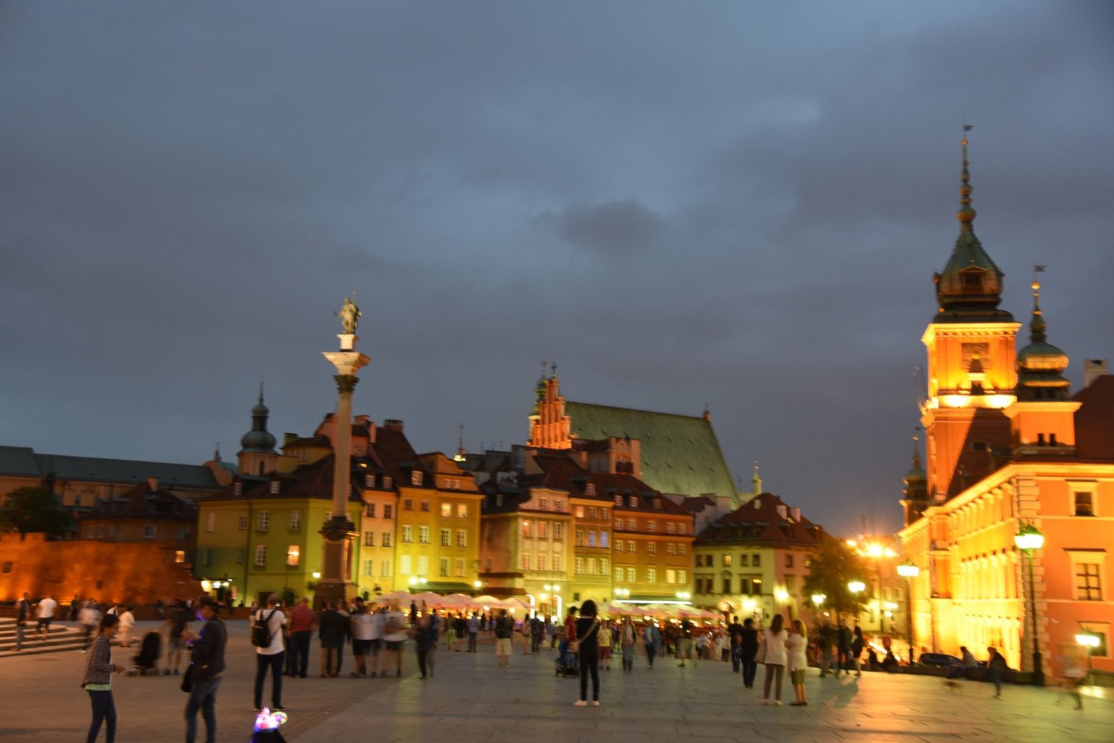 Castle Square at dusk, with Sigismund's Column, the lit houses of the Old Town and the Royal Castle's clock tower glowing orange