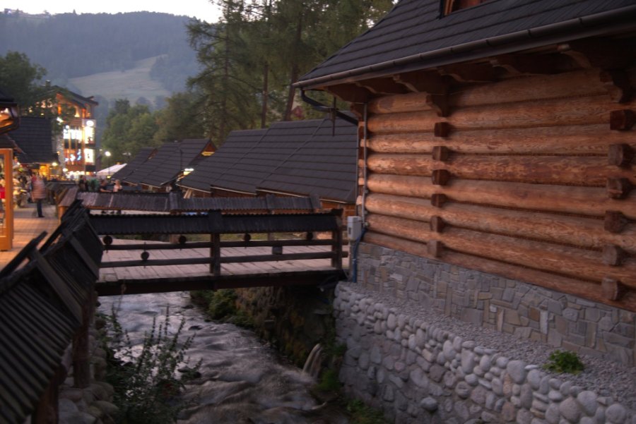 A log-built house and a wooden footbridge over the stream on Krupówki at dusk