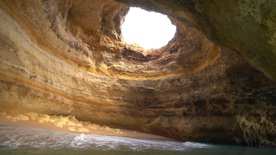 Daylight falling through the round hole in the roof of the Benagil cave onto the beach inside