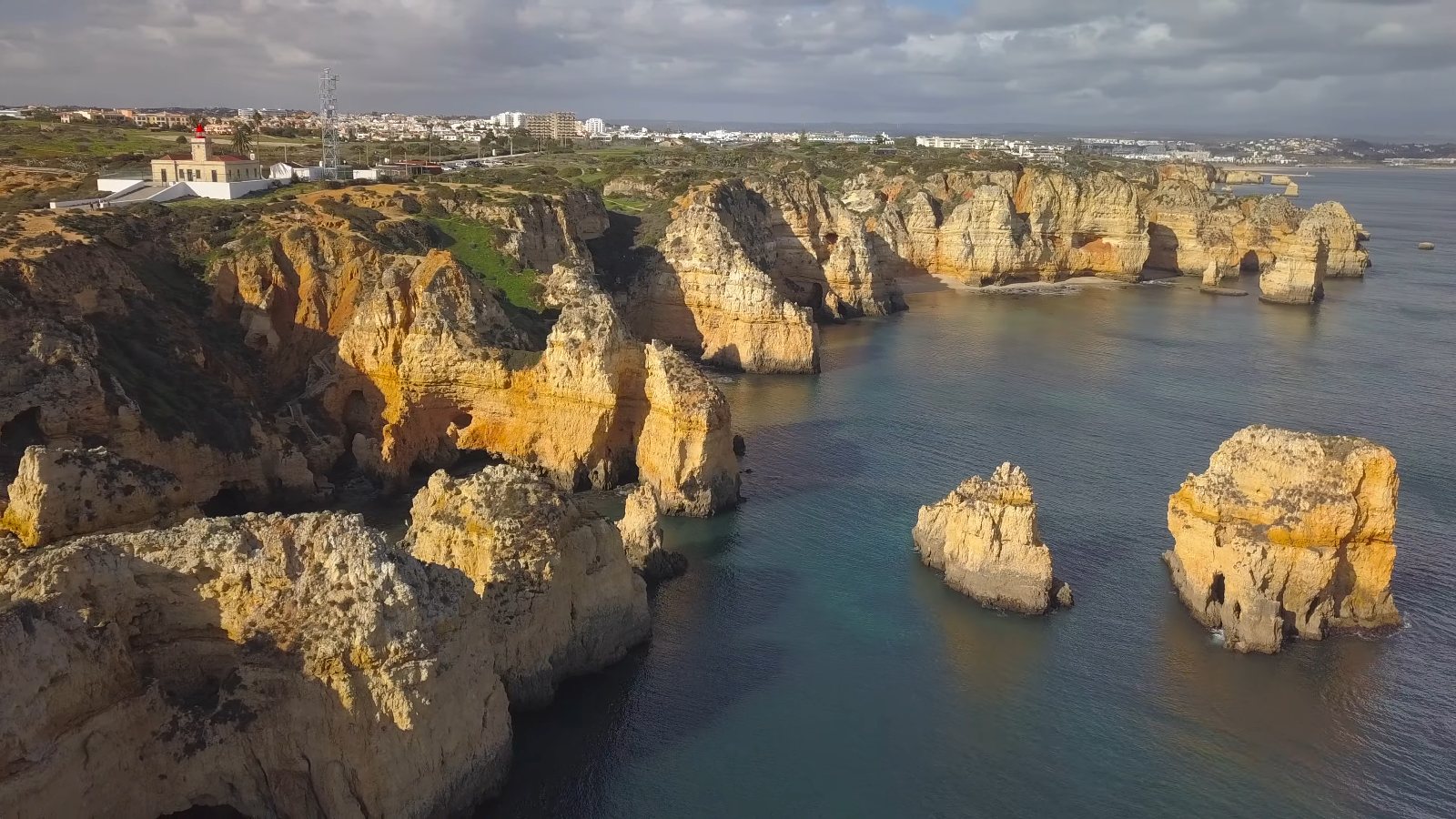 Drone view of Ponta da Piedade's golden cliffs and sea stacks, with the lighthouse on the headland