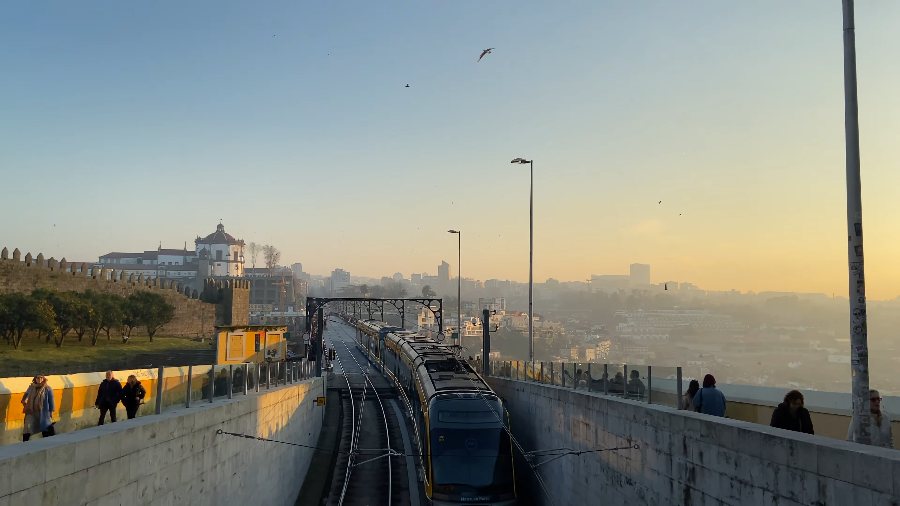 Sunset on the top deck of the Dom Luís I bridge as a metro train passes, with the Serra do Pilar monastery on the hill