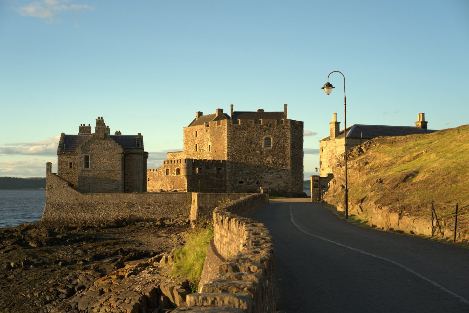 Blackness Castle's stone walls and towers lit gold by the low sun, beside the road and an old lamppost