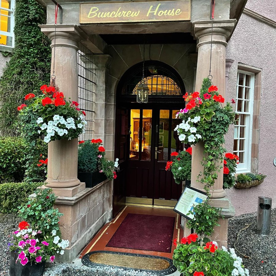 The arched front door of Bunchrew House under its name, framed by red and white flowers