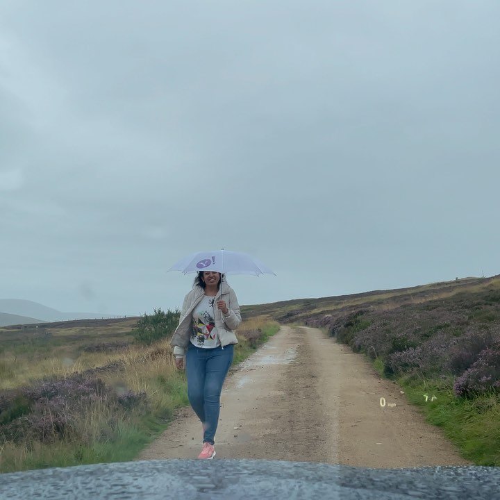 Meenu walking down a track across the moor under an umbrella