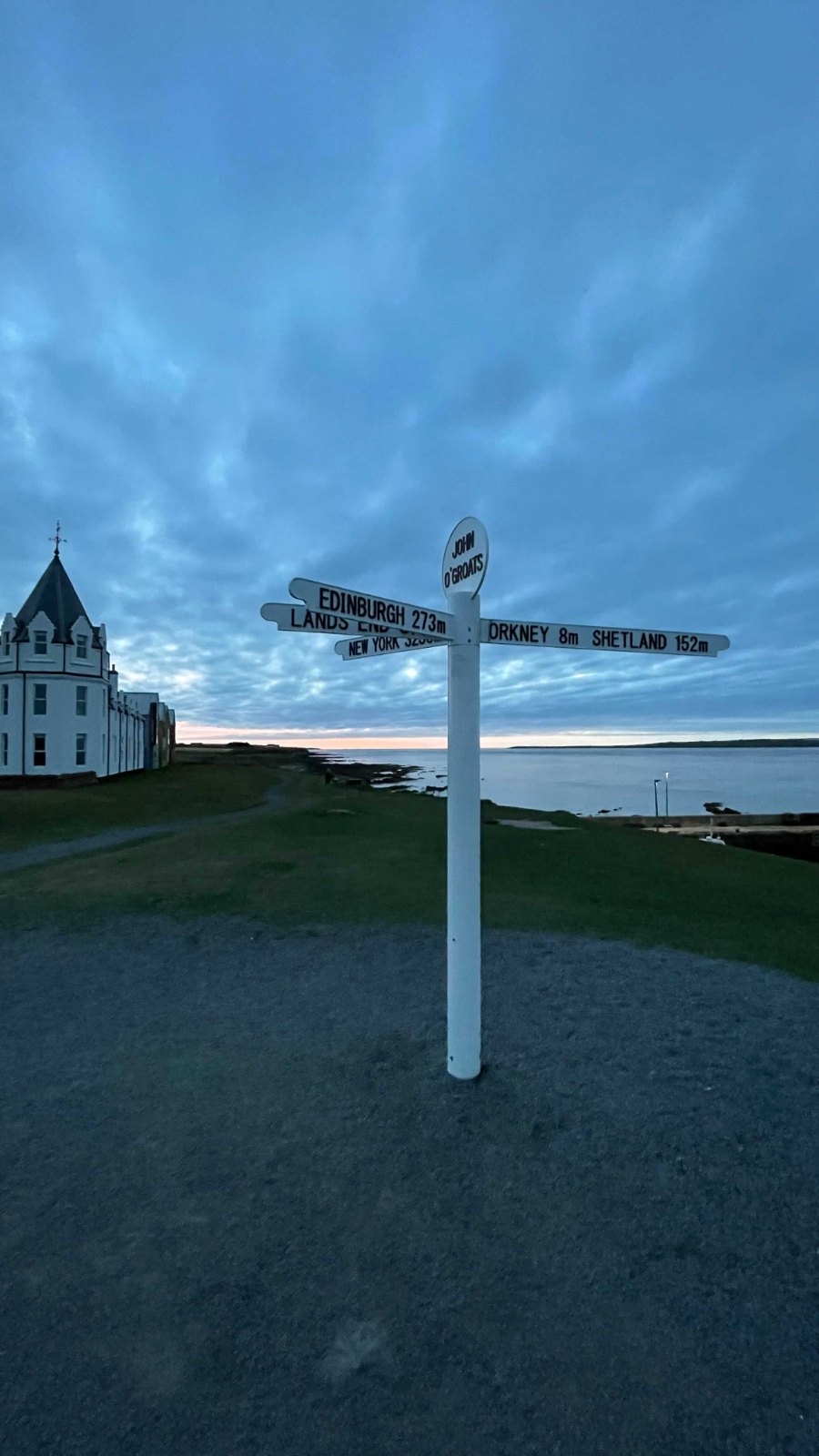 The white signpost at John o' Groats, with the sea and a white building behind