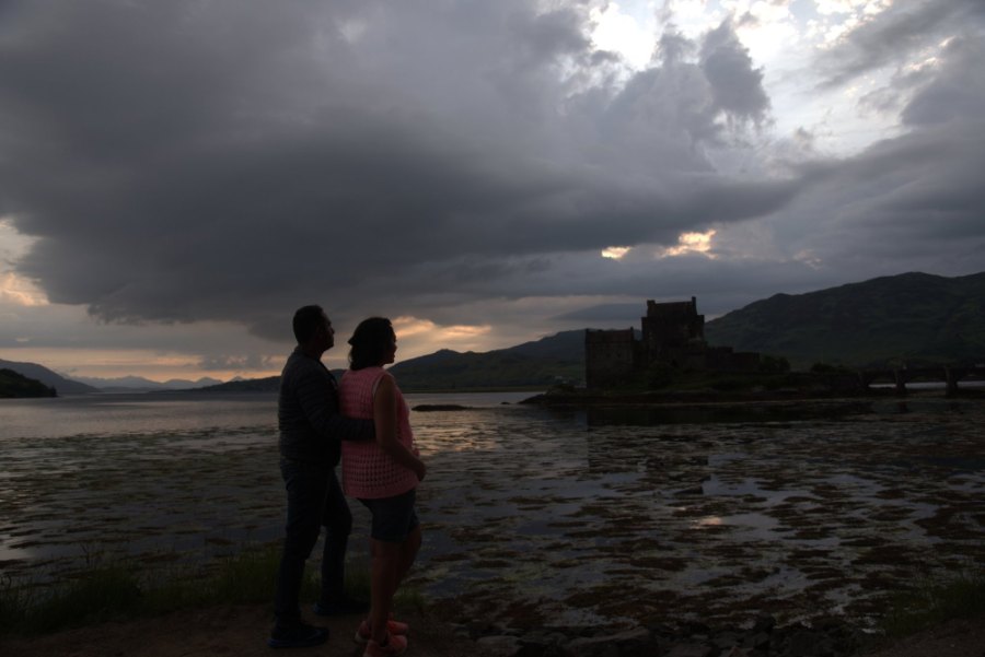 Praddy and Meenu in silhouette on the shore, with Eilean Donan under dark clouds