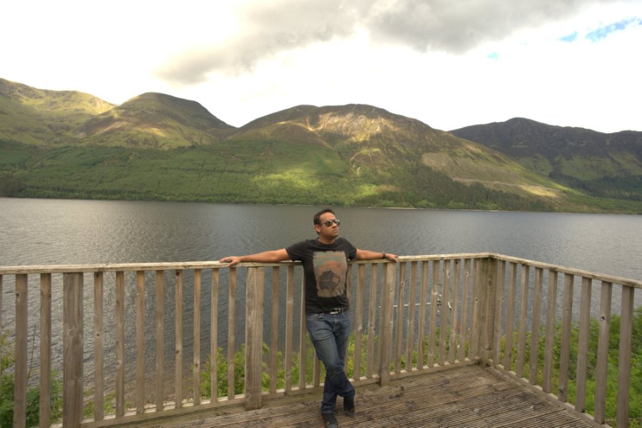 Praddy leaning on the deck rail at Letterfinlay, with Loch Lochy and sunlit hills behind
