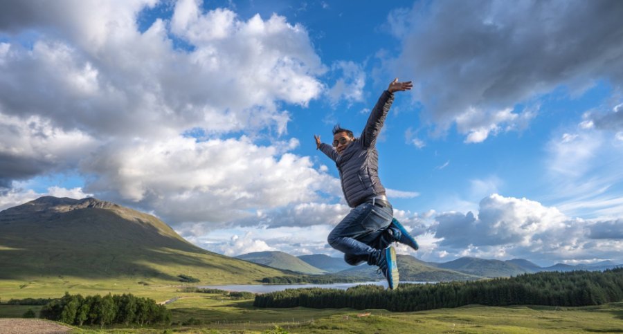 Praddy leaping in the air at the viewpoint above Loch Tulla, under a blue sky full of cloud
