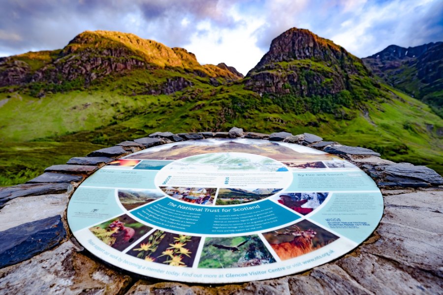 The Three Sisters of Glen Coe behind the round information table at the viewpoint