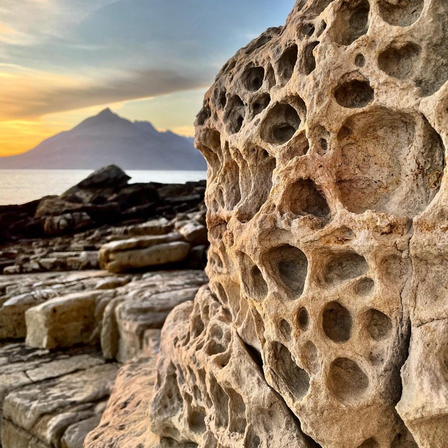 Honeycombed rock on the shore at Elgol, with a pointed mountain across the water at sunset
