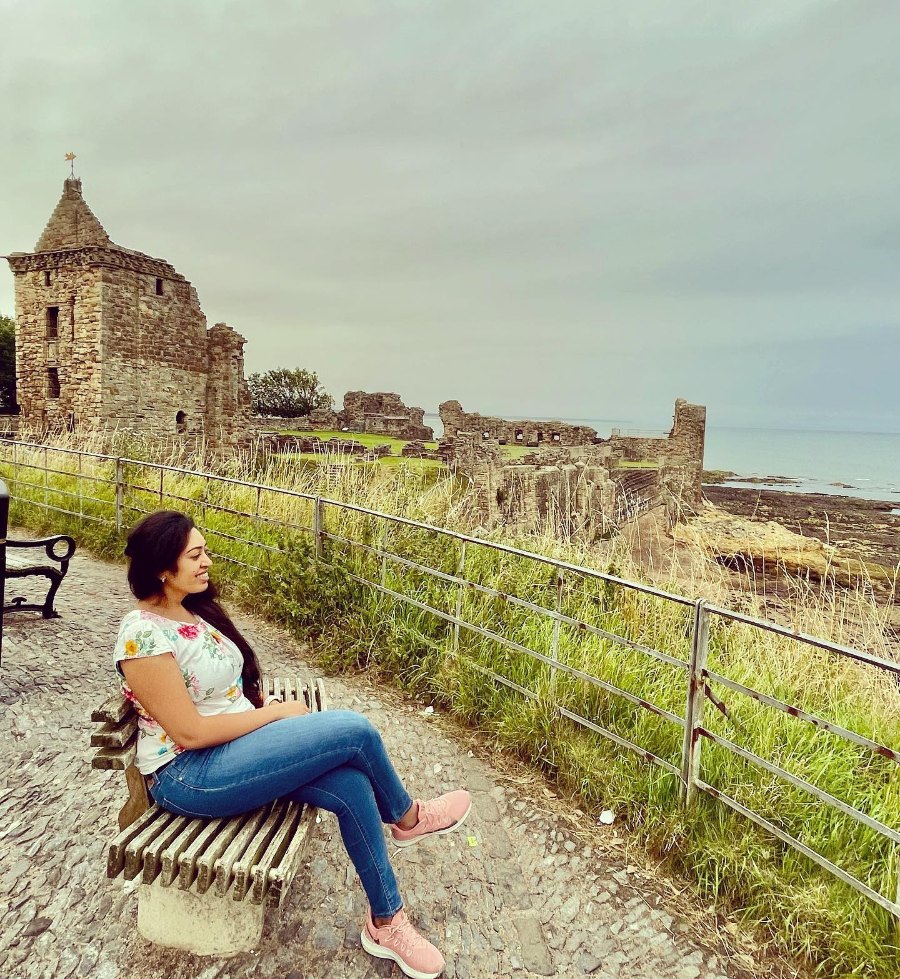 Meenu sitting on a bench beside the castle ruins in St Andrews