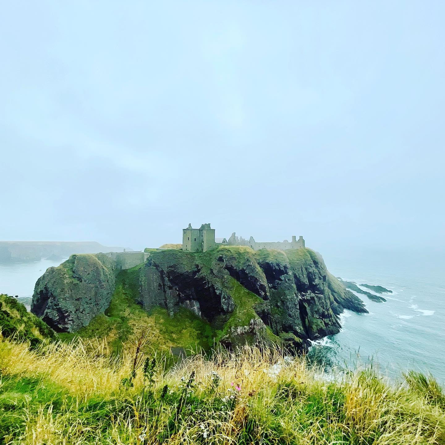 Dunnottar Castle's ruins on top of a sheer green headland, half lost in sea fog
