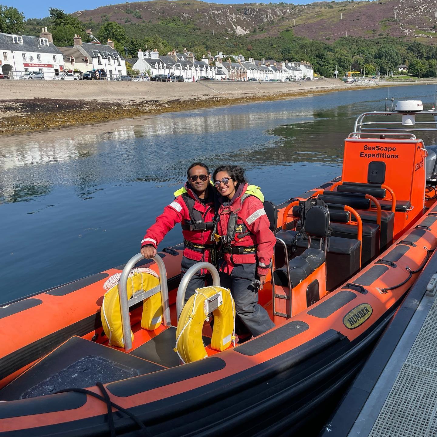 Meenu and Praddy in red survival suits on an orange RIB in Ullapool's harbour